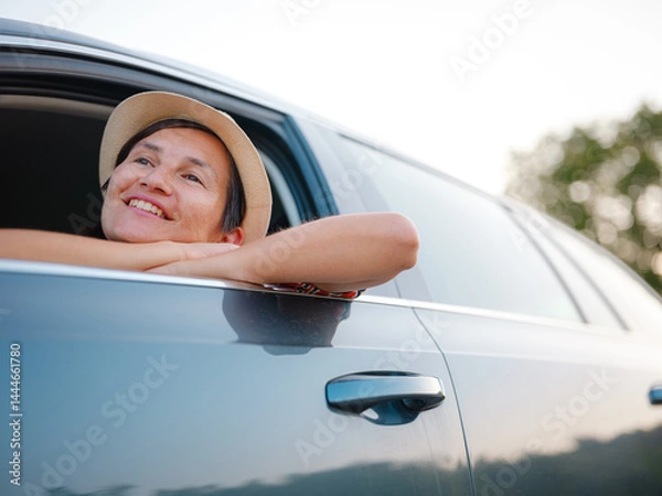 Fototapeta Traveler woman in red ethnic dress and hat drives car through scenic countryside of Croatia in summer. Surrounded by lush fields and forests, she enjoys peaceful and adventurous road trip