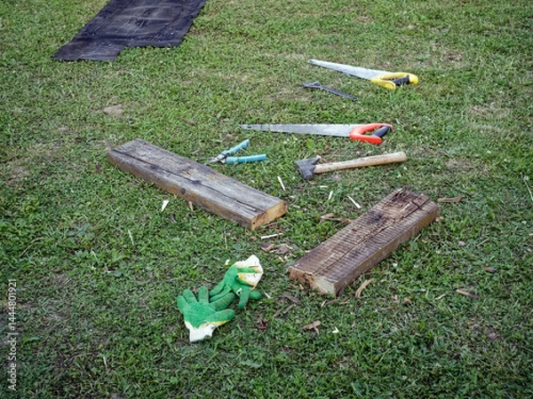 Obraz Saws, axes and planks lie in front of a rural house
