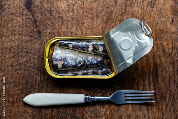 Fototapeta Open tin can of sardine fish and fork on wooden table background, closeup, top view