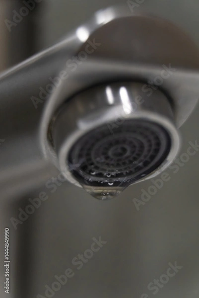 Fototapeta Close-up of a dripping faucet with a single drop of water forming, highlighting the importance of water conservation and the need to fix leaks to prevent water waste. Vertical photo
