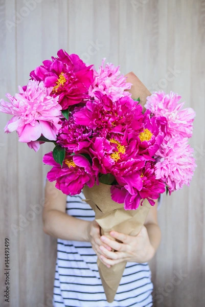 Obraz happy white caucasian girl holding red and pink peonies bouquet in front of face at wood wall backdrop