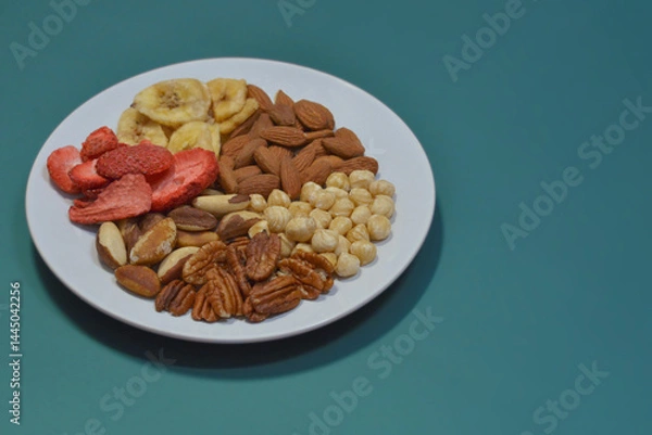 Fototapeta A variety of nuts and dried fruits on a plate on blue background. Hazelnuts, pecans, brazil nuts, almonds, dried strawberries and bananas. The concept of nutrition, diet, healthy eating and sports