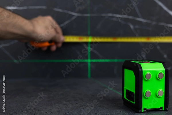 Fototapeta hands of a worker who measures the width of a tabletop with a tape measure and a laser