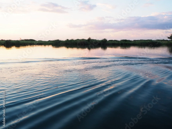 Fototapeta Sunset scene at the river bank with water ripple and reflection