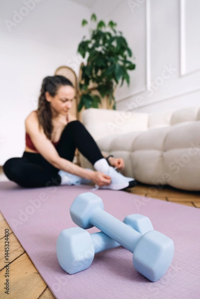 Fototapeta Woman engages in fitness exercise at home on a yoga mat with dumbbells nearby