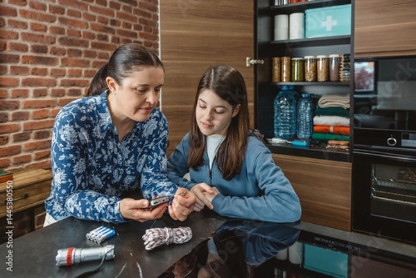Fototapeta Mother and daughter listening emergency news in small portable radio receiver during electrical blackout. 72 hours survival kit stored for disasters. Alert, foresight and self sufficiency strategy.