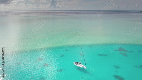Fototapeta A stunning view sailboat gently bobbing on crystal clear turquoise waters. Surrounding the boat, vibrant coral reefs are visible beneath the surface, inviting exploration, peaceful tropical day.