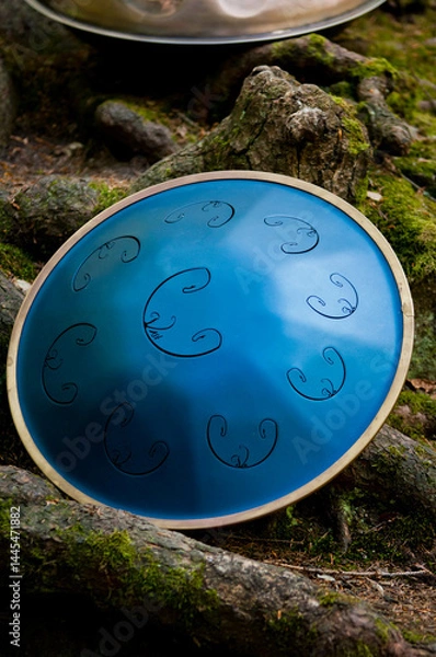 Fototapeta Portrait of a musician playing a handpan outdoors near a waterfall, captured in natural light. The image highlights the unique shape and texture of the handpan instrument, symbolizing mindfulness, rhy