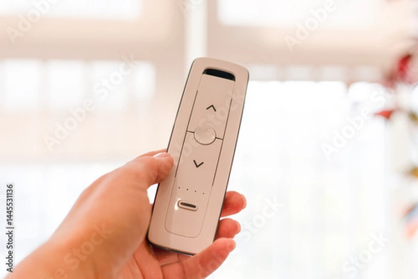 Obraz Radio remote control panel for blinds and roller shades in woman hand, white, close-up. Bright background. Blinds and curtains for smart house. Home automation, wireless technology. Electronic device.