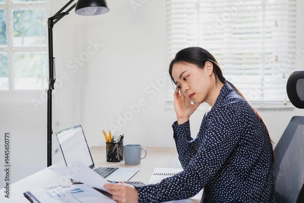 Fototapeta Businesswoman sitting at desk on couch in workplace or at home working on laptop and analyzing data on charts and graphs and writing on papers to make business plan and strategies for company, 