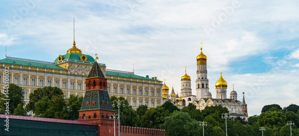 Obraz Picturesque view of Moscow's Kremlin towers rising above lush green trees, with historic architecture under clear blue sky