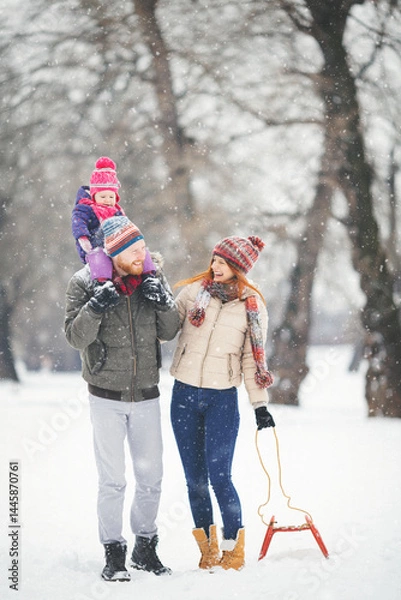 Fototapeta Young family with baby girl having fun in the snow