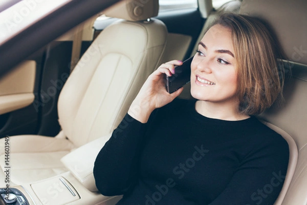 Fototapeta Close-up portrait of beautiful happy and laughing with all teeth young Caucasian woman is sitting in car and talking on mobile phone. Lifestyle, traveling and communication concept.