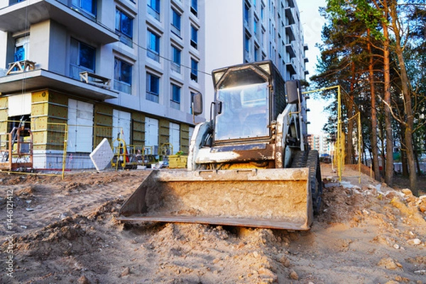 Obraz Skid steer loader on construction site. Compact Track loader, construction equipment. Road repair at construction site. Bobcat skid-steer loader on roadworks. Building construction work. Renovation.