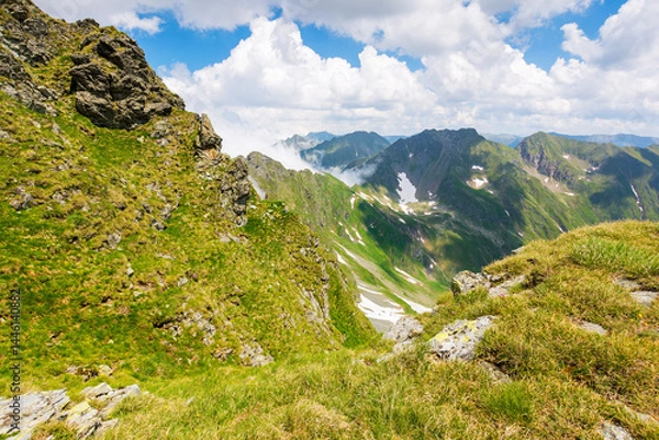 Fototapeta alpine landscape of romania in summer. vacation season. fagaras mountain ridge on a sunny day. scenic valley with snow on the grassy slope beneath a blue sky with clouds. travel to transylvania