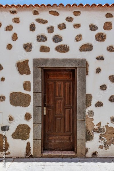 Obraz Rustic wooden door in stone wall facade, Old wooden door set in a whitewashed wall with exposed natural stones.