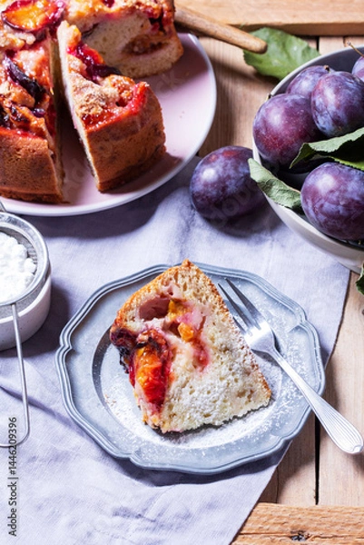 Fototapeta Plum pie with filling and sugar crust, sprinkled with powdered sugar and plums on a wooden table.