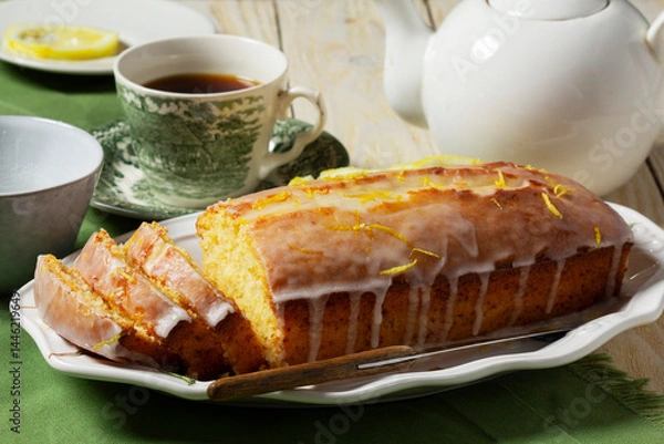 Fototapeta Aromatic lemon cake, covered with sugar icing and sprinkled with zest, served with tea.