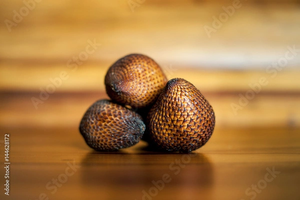 Fototapeta Three ripe whole salak or shake fruits lying on wooden background. Exotic fruits