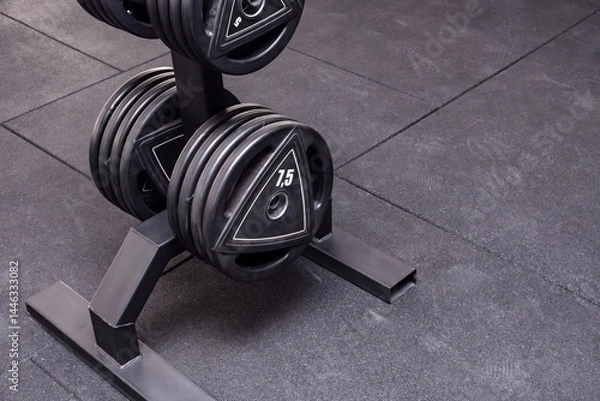 Fototapeta Barbell disks on a rack in a modern gym. A close-up view of a set of barbell disks neatly placed on a sturdy rack.