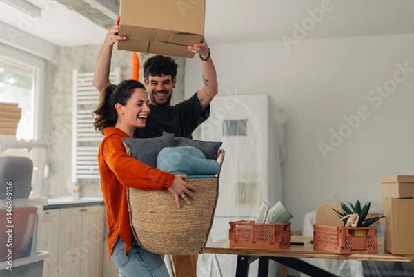 Fototapeta Happy couple carrying boxes and baskets while moving into new home