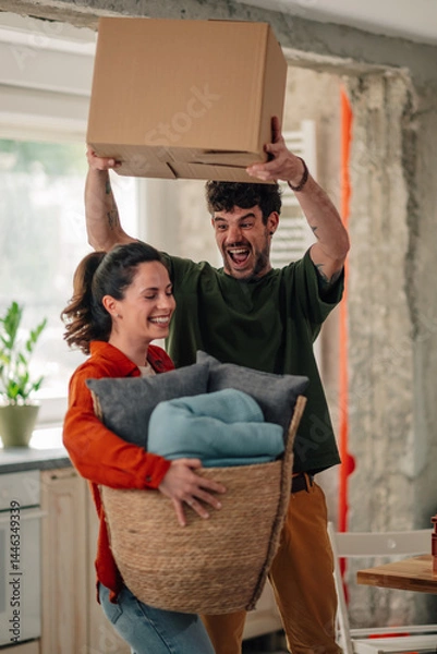 Fototapeta Happy couple carrying boxes and baskets while moving into new home
