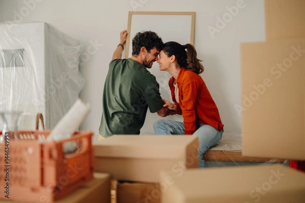 Fototapeta Happy couple hanging a picture frame in new home while moving in