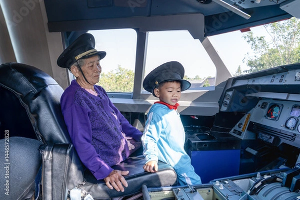 Fototapeta Grandmother and grandson at controls of airplane sitting in cockpit wearing a pilot hat and sitting in an airplane cockpit, smiling confidently, portraying dreams of aviation and  future of flight.