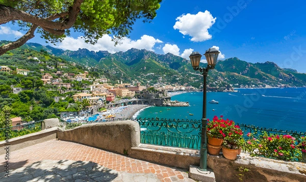 Fototapeta Coastal town panorama. Cliffside buildings overlook a beach and blue ocean under a clear sky with greenery