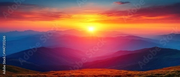 Fototapeta Bright sun setting over mountain peaks with colourful sky and foreground grass