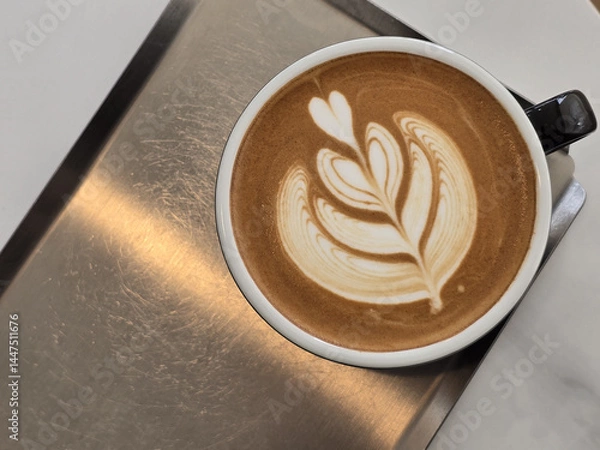 Obraz beautifully crafted latte with intricate foam art sits in black cup on metallic surface, showcasing heart and leaf design that adds artistic touch to beverage