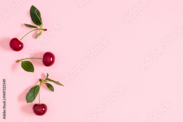 Fototapeta Border of ripe cherry berries with leaves, pattern of leaves and cherries, on a pastel pink background, top view