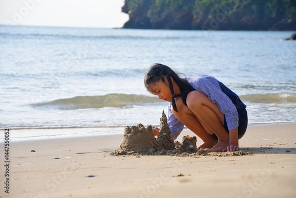 Fototapeta A girl is playing in the sand on the beach.