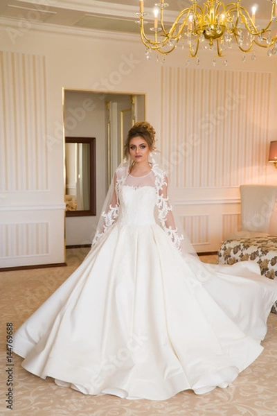 Fototapeta Portrait of beautiful young bride. A girl is posing in a hotel room. A lady Is worth with by the window. bride waiting in hotel.