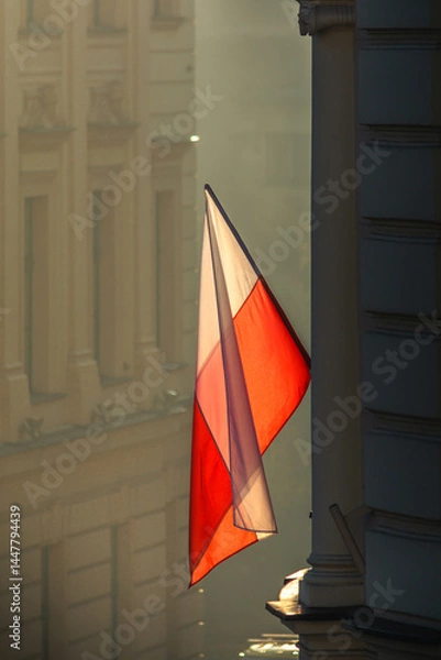 Obraz Biało-czerwona flaga Polski oświetlona wschodzącym słońcem na budynku podczas święta państwowego