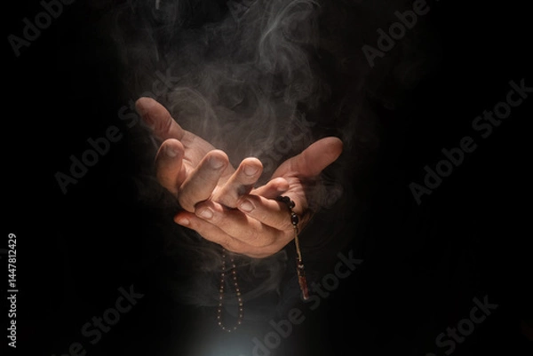 Fototapeta Hands in prayer, Hands of a person in prayer with a rosary in a dark and smoky place, low key portrait, selective focus.