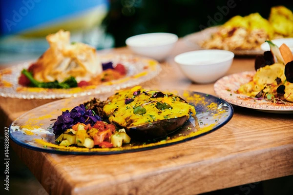 Obraz A plate of food with a yellow sauce on it. The plate is on a wooden table. There are other plates of food on the table as well