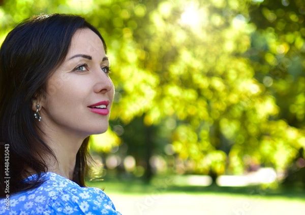 Fototapeta Portrait in profile of a beautiful woman with a smile on the background of nature. copy space