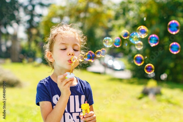 Obraz A little girl blowing soap bubbles in summer park. Background toninf for instagram filter.