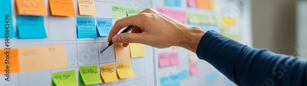 Obraz Hand Placing Sticky Notes on a Colorful Project Management Board