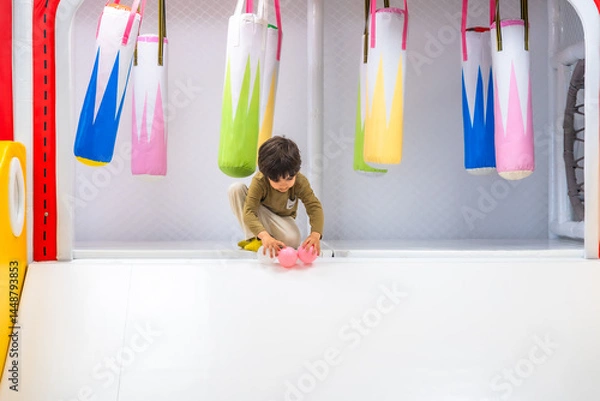 Fototapeta Boy playing with balls in soft play area with punching bags