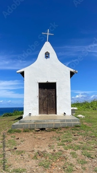 Fototapeta Saint Peter Chapel, a tiny whitewashed chapel built by fisherman on the top of a mound. Blue sky, white clouds, green lawn. Fernando de Noronha island, Brazil. Sunny day, beautiful view. Cirrus clouds