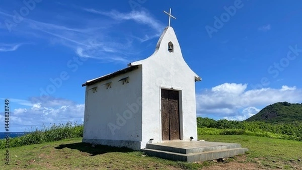 Fototapeta Saint Peter Chapel, a tiny whitewashed chapel built by fisherman on the top of a mound. Blue sky, white clouds, green lawn. Fernando de Noronha island, Brazil. Sunny day, beautiful view. Cirrus clouds