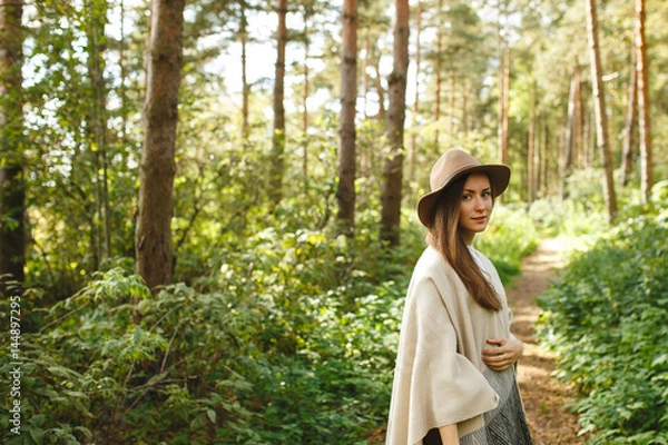 Fototapeta A girl in a poncho and a hat in forest