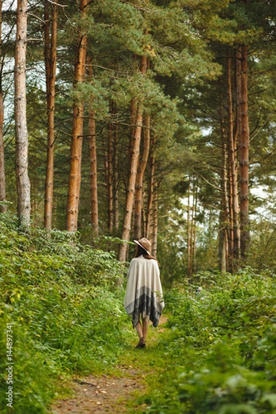 Fototapeta A girl in a poncho and a hat in forest