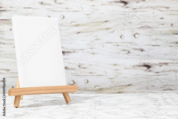 Fototapeta Vertical blank canvas on an easel on a marble table in front of a wooden background. Minimalist concept for art or design
