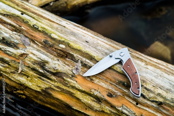 Fototapeta Folding knife on a log laying over a stream
