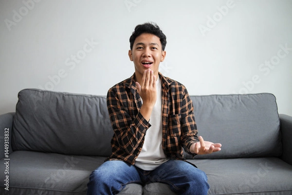 Obraz Man showing THANK YOU gesture in sign language while sitting on a couch