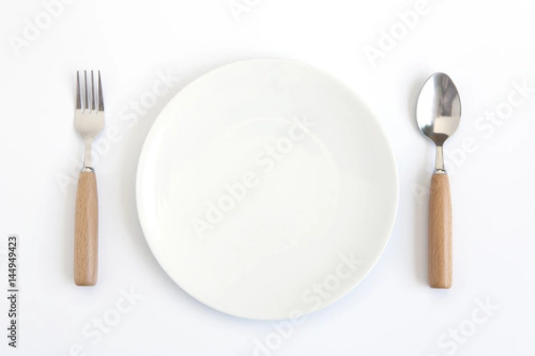 Obraz A white plate with fork and spoon on white background.