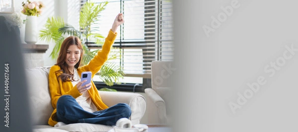 Fototapeta Happy young asian woman using mobile apps in living room,Smiling young asian female using smartphone sitting on couch at home.Messaging,Online Shopping,celebrate success,chatting online,Social Media

